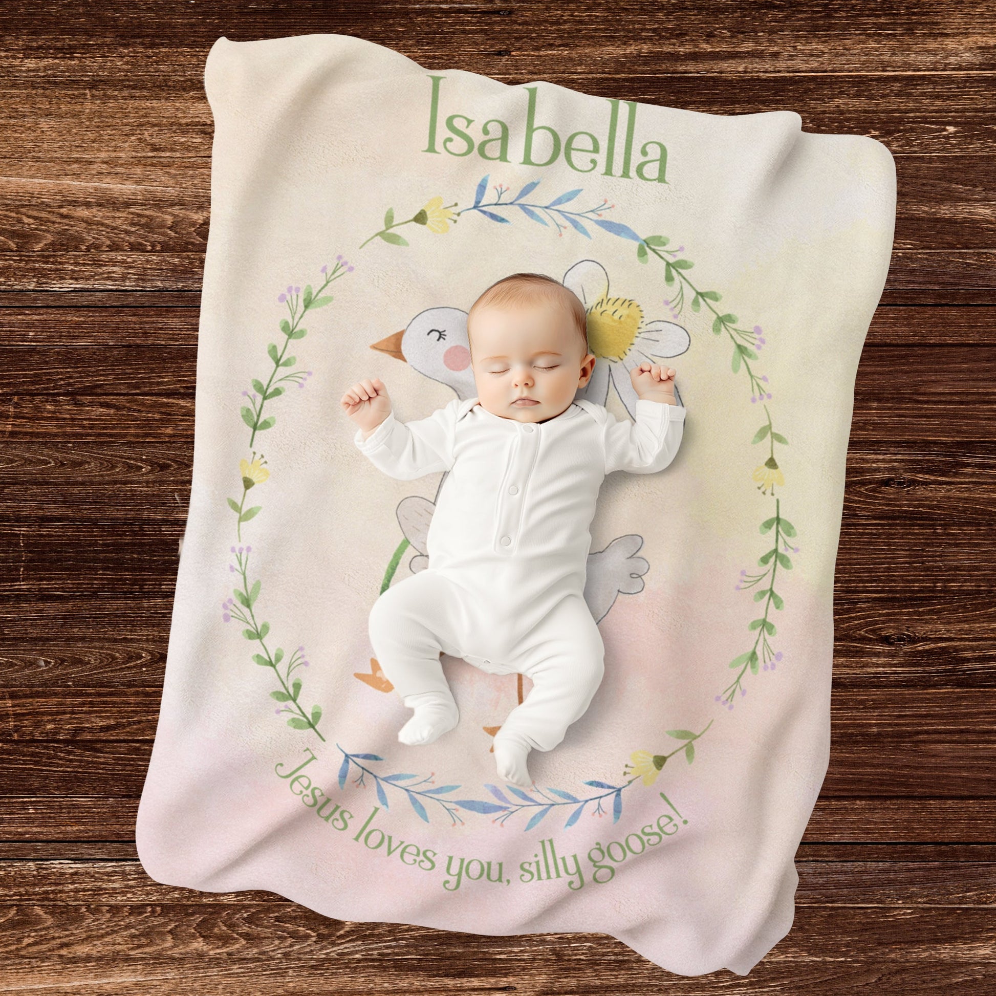 Baby lying on a personalized blanket with cartoon goose design and text on a wooden surface